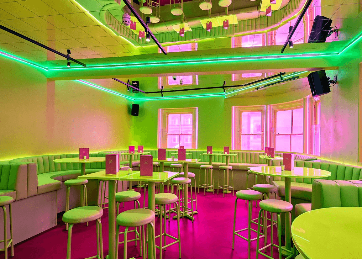 A pink and green themed bar area with booth and table seating